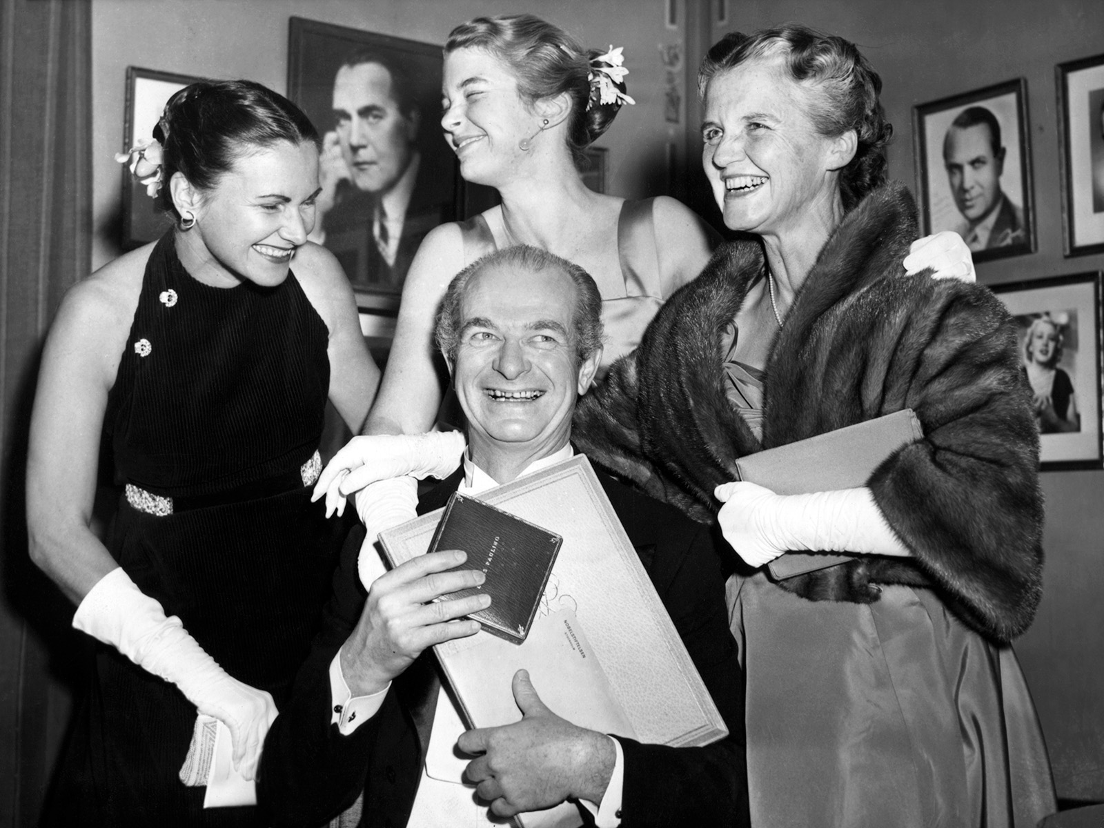 Celebration scene of older seated man surrounded by three standing women, all in formal wear