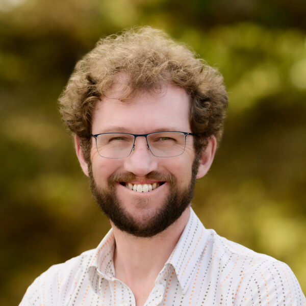 man, smiling, outdoors, wearing glasses and white collared shirt with light vertical stripes