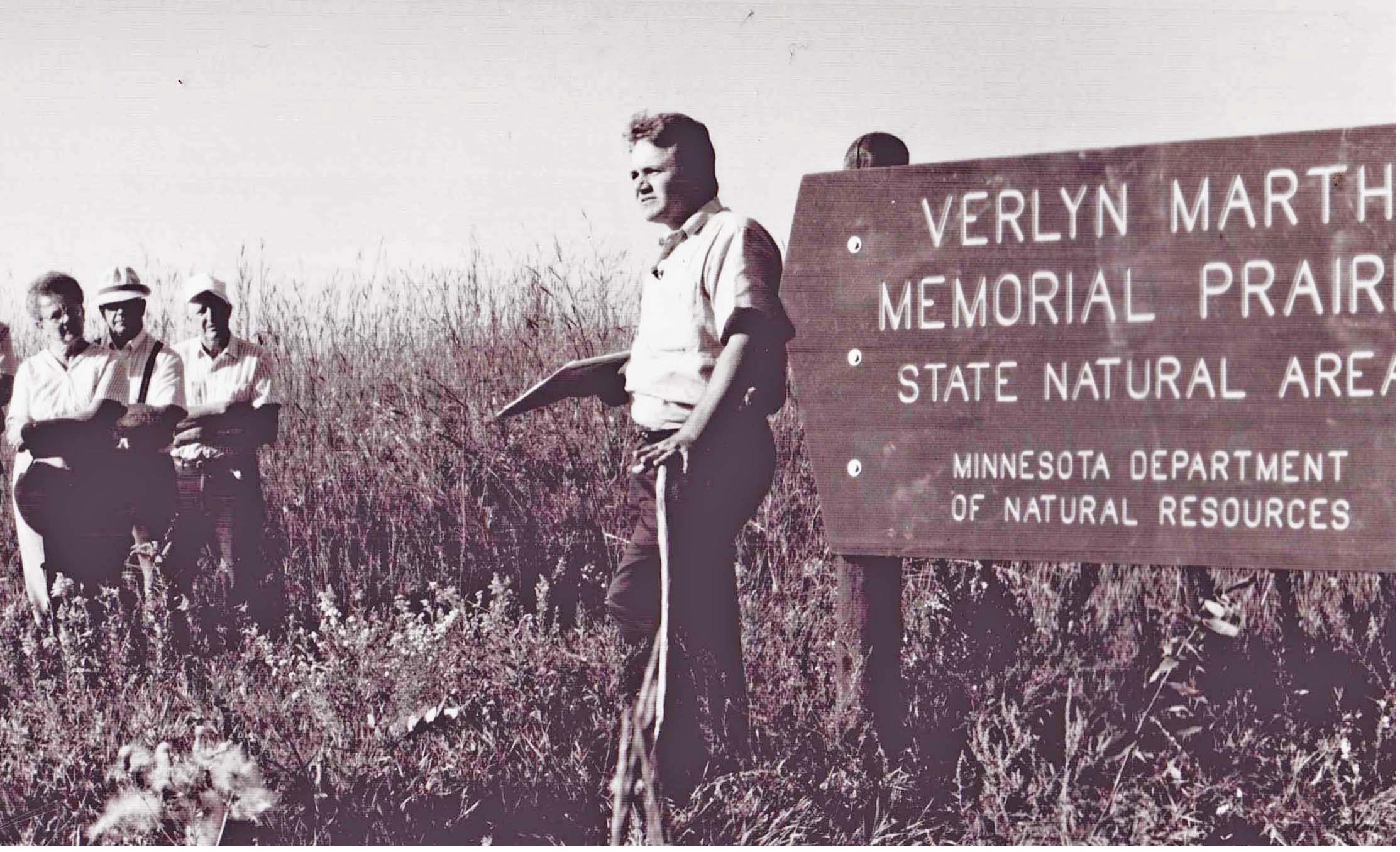 man standing in field next to a state park sign