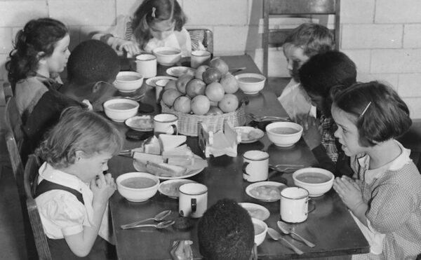 Black and white photo of school children sitting around a table eating lunch