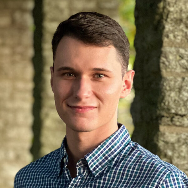 man in checked collared shirt amid stone colonnade