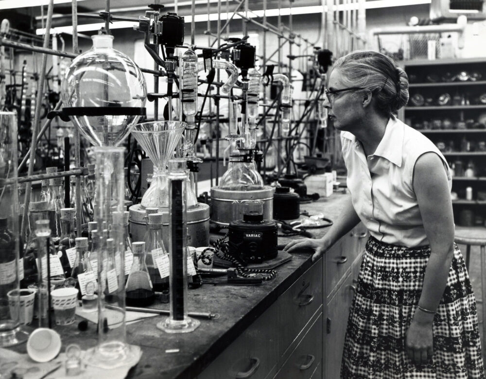 woman wearing glasses and plaid skirt in front of lab glassware