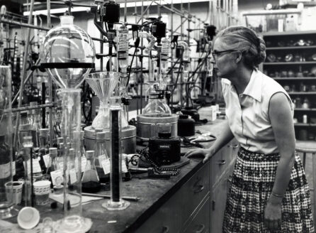 woman wearing glasses and plaid skirt in front of lab glassware