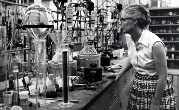 woman wearing glasses and plaid skirt in front of lab glassware