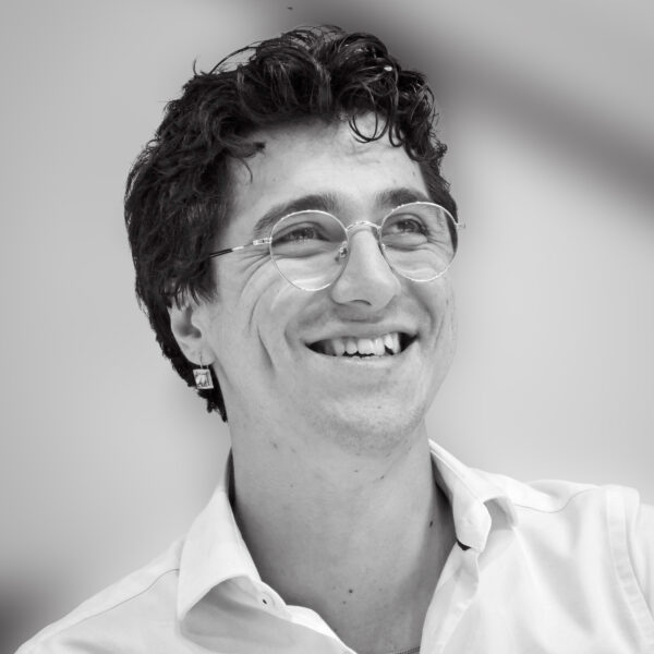 black-and-white photo of a man, smiling, in white shirt with glasses and earring