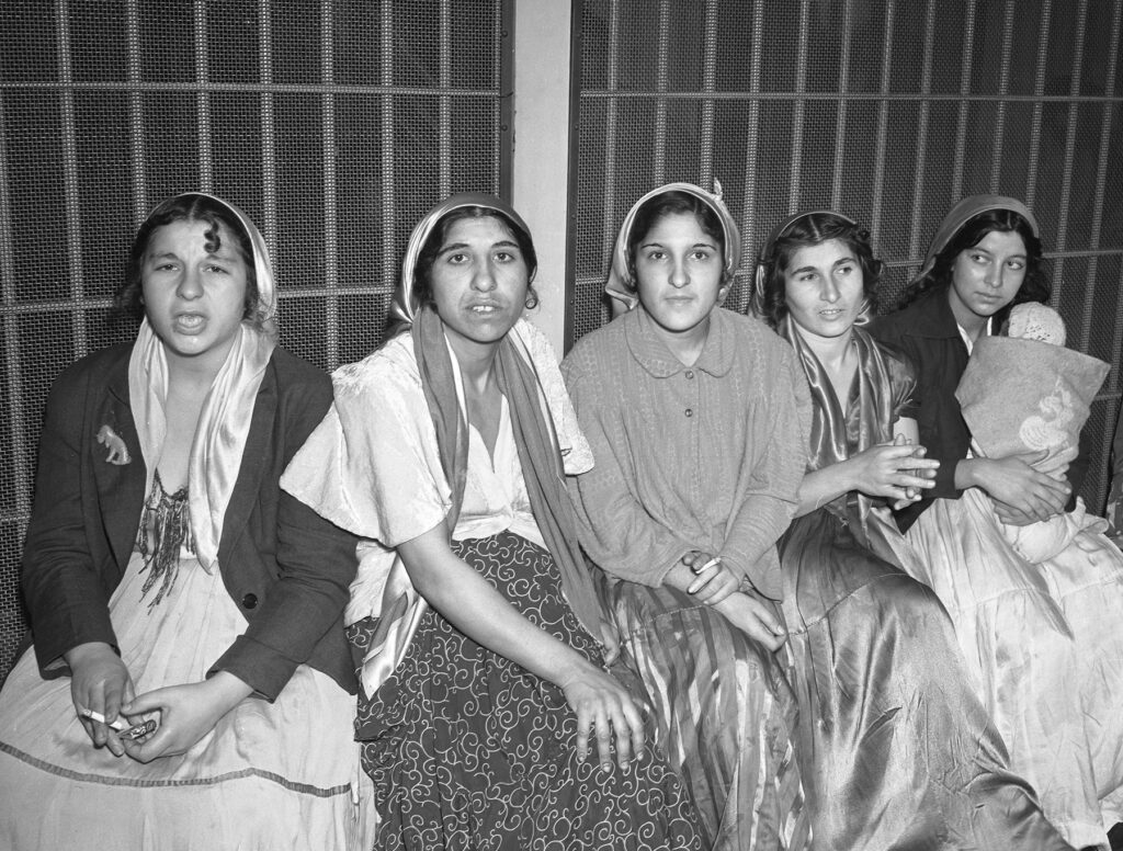 Black and white photo of six women seated in a jail cell