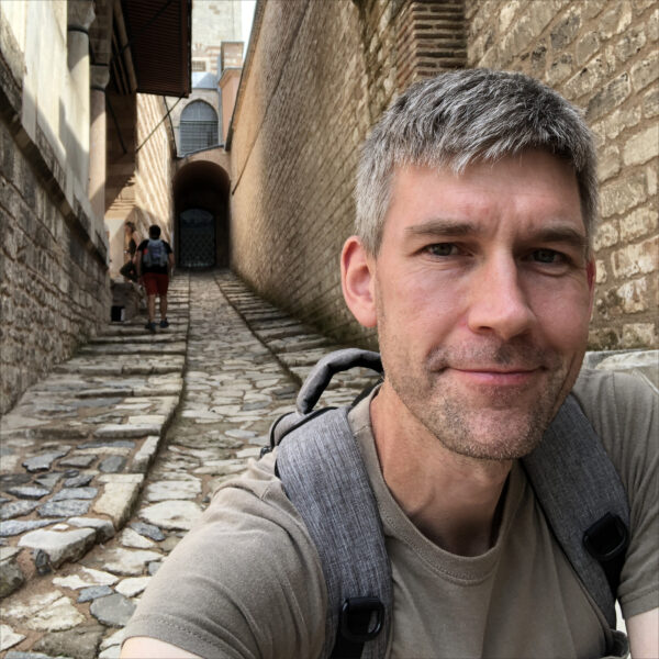 Sam Kean with backpack and T-shirt in a Southern European passageway