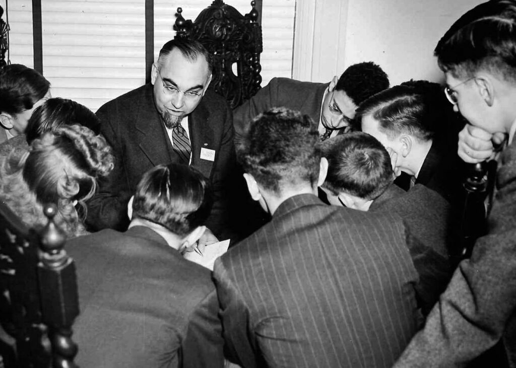 A black and white photo of a man surrounded by young people sitting at a table