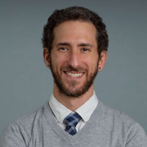 studio portrait of man with beard, wearing a sweater over shirt and tie