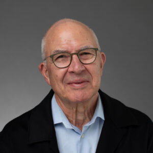 studio portrait of a main with glasses, light blue dress shirt, and black jacket