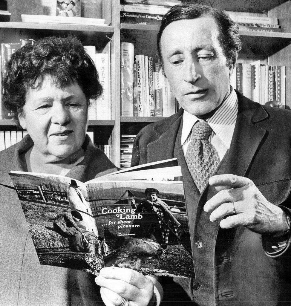 A black and white photograph of a man and woman holding and reading from a book, with a bookshelf in the background. The book’s title reads: “Cooking Lamb for Sheer Pleasure.”