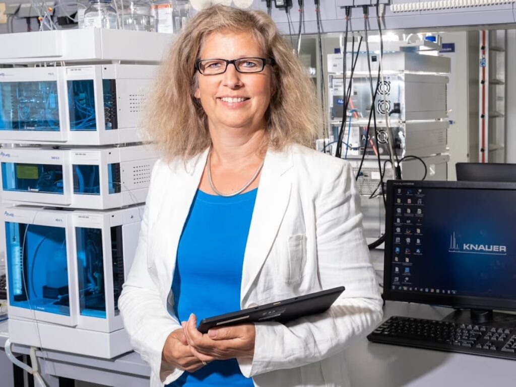 Woman in lab environment with a tablet, glasses, blue shirt, and white blazer