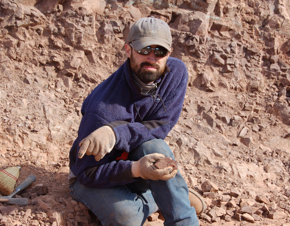 Man crouching on a rocky hillside, holding a sample