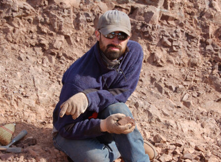 Man crouching on a rocky hillside, holding a sample