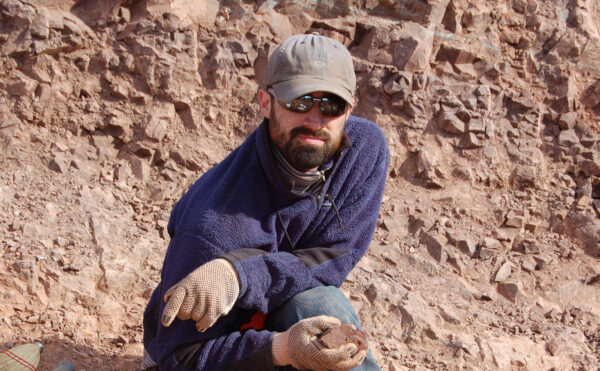 Man crouching on a rocky hillside, holding a sample