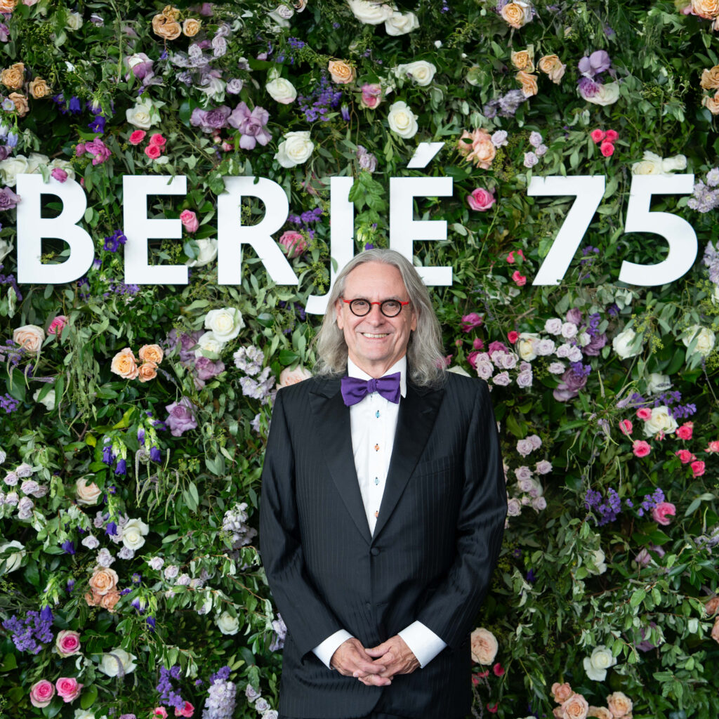 Kim Bleimann in tuxedo in front of a floral wall that says Berjé 75