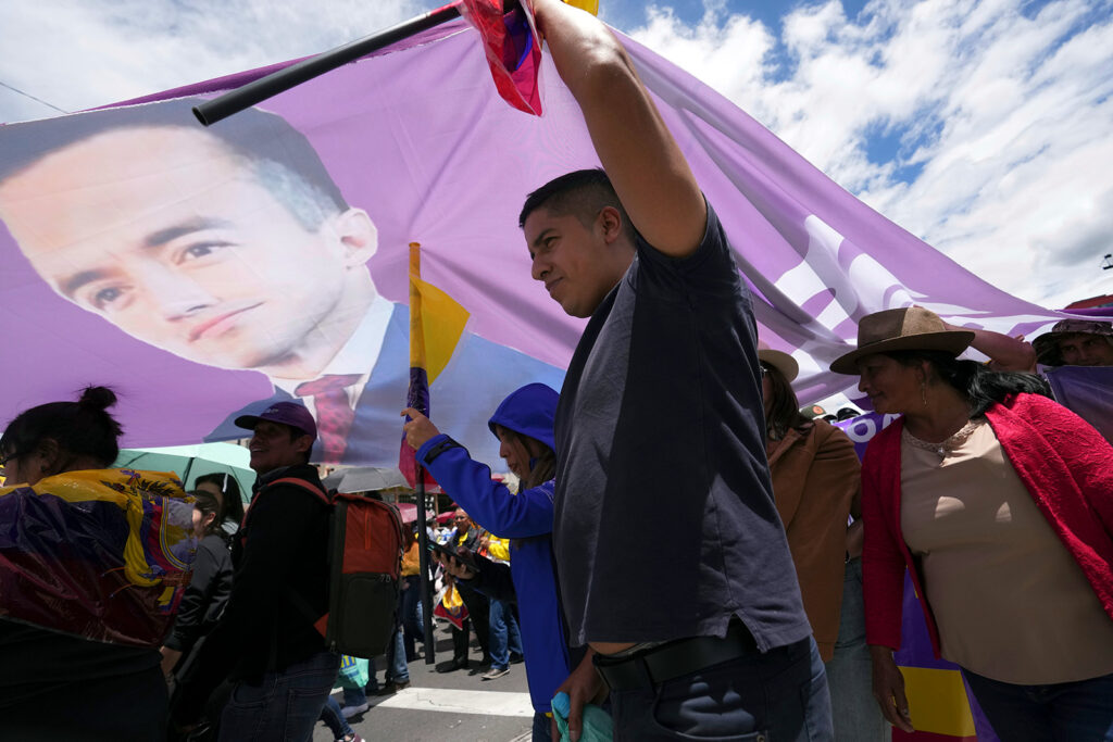 color photograph of a marching crowd waving a large purple flag with the face of President Daniel Noboa on it