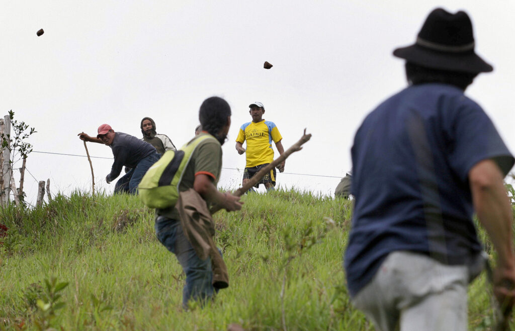 color photograph of men holding sticks and throwing stones at each other on a hillside