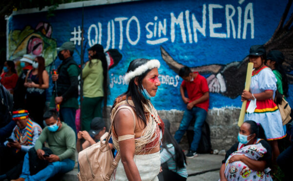 A color photo of a woman in a crowd walking past a painted blue wall with street art that reads: Quito sin minería (Quito without mining).