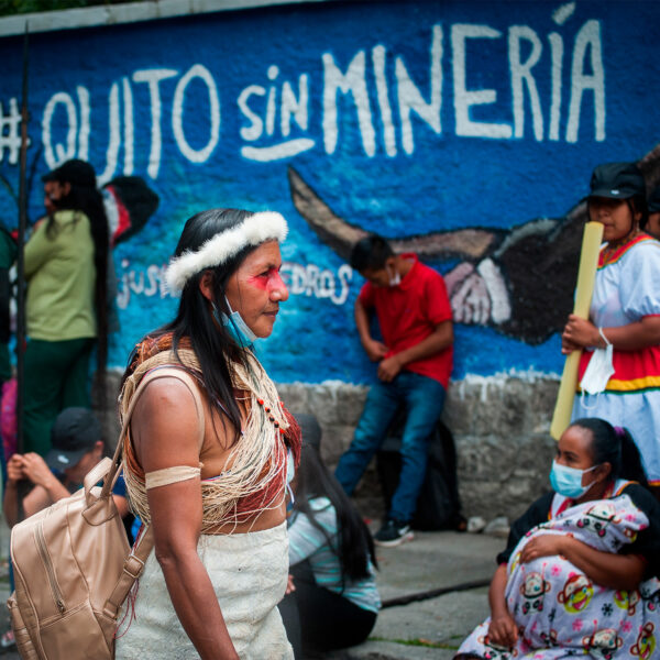 A color photo of a woman in a crowd walking past a painted blue wall with street art that reads: Quito sin minería (Quito without mining).
