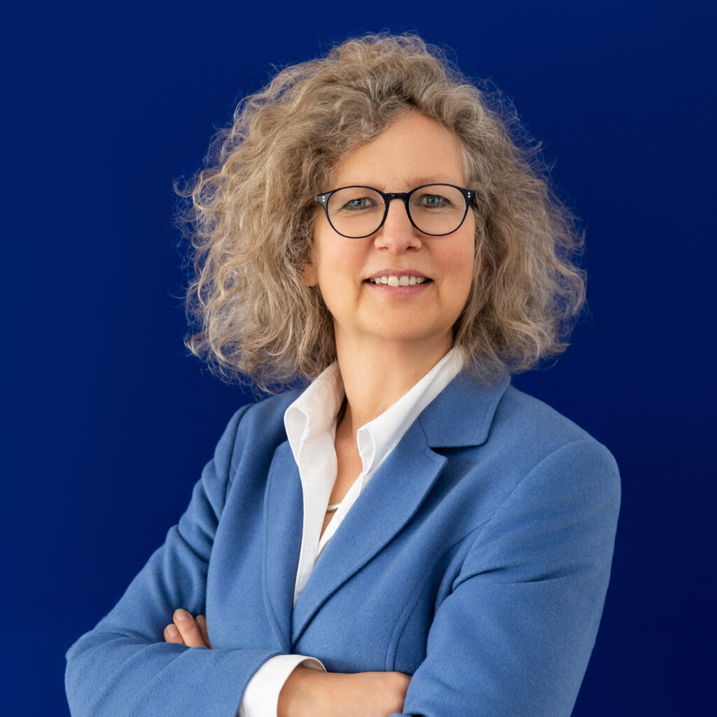 Studio portrait of Alexandra Knauer wearing light blue jacket over dark blue backdrop