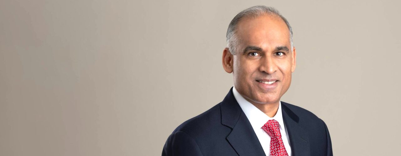Studio portrait of Bob Patel wearing black blazer, white shirt, and red tie