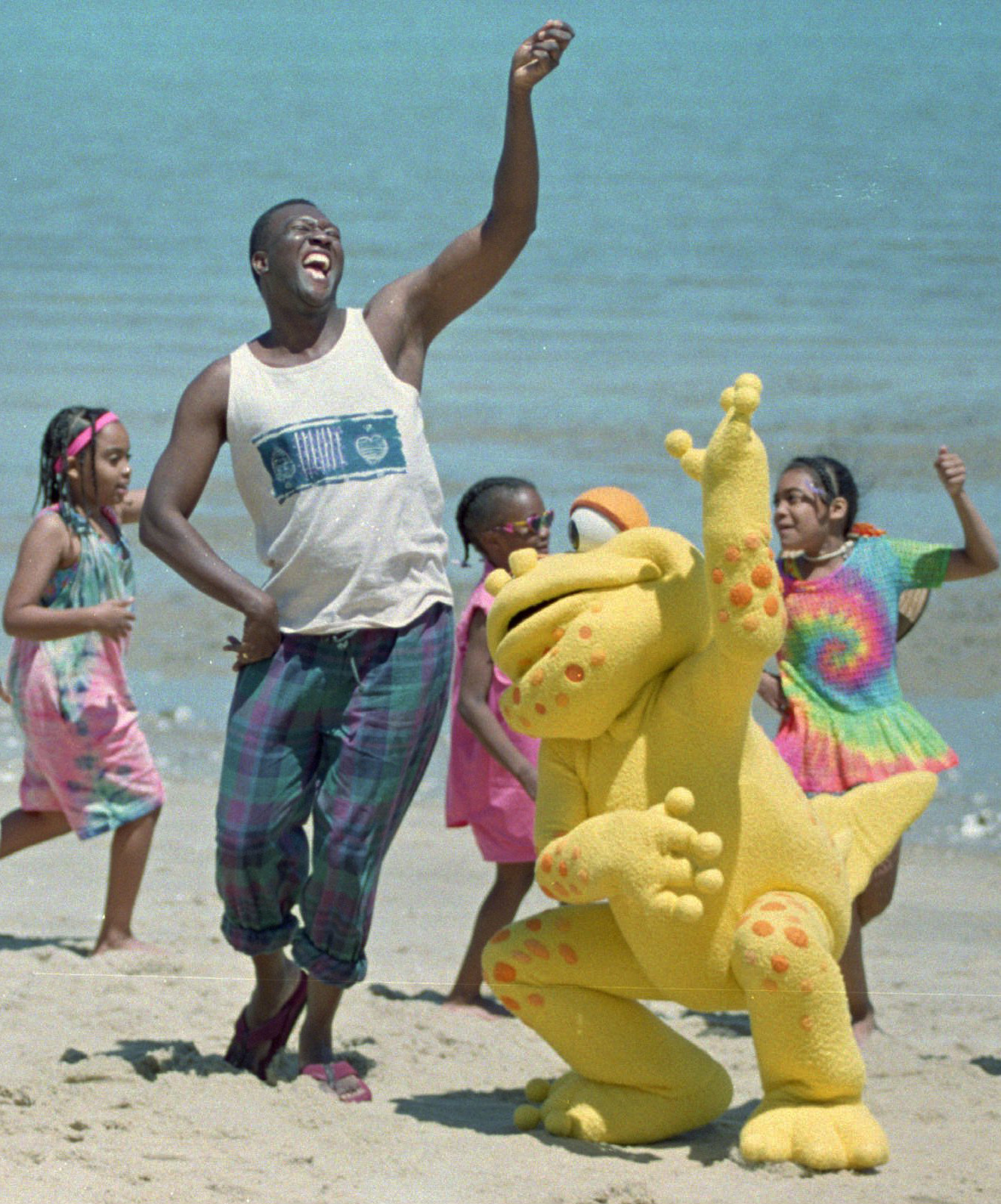 Un hombre y tres niños bailan junto una gran marioneta de rana