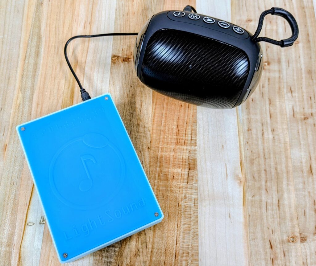Rectangular blue plastic box connected to a small speaker by an audio cord.