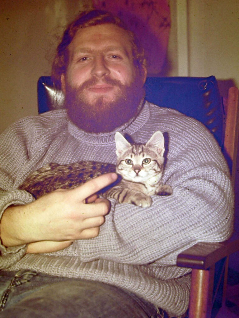 A seated man holding a tabby kitten