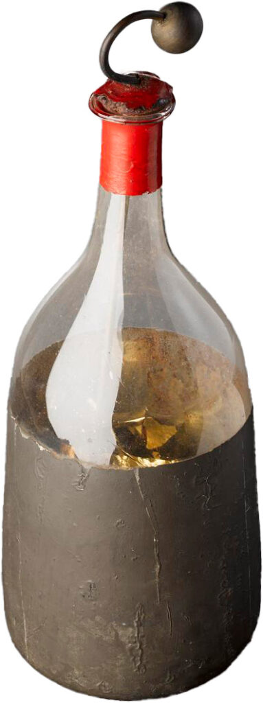 A glass jar with the bottom half lined with gold leaf and a red stopper at the opening. A metal rod is inserted into the jar