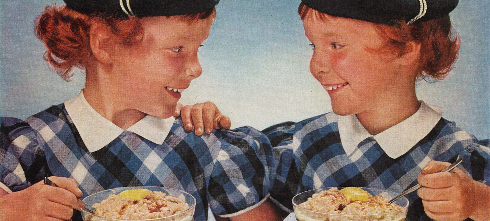 Twin girls in Scottish costumes eating bowls of oatmeal at a table