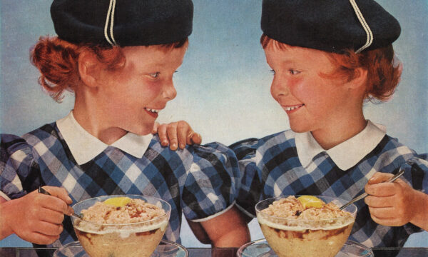 Twin girls in Scottish costumes eating bowls of oatmeal at a table