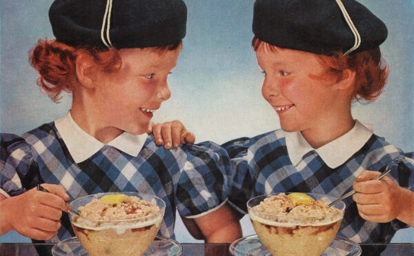 Twin girls in Scottish costumes eating bowls of oatmeal at a table