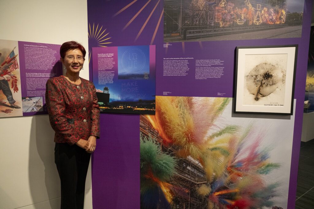 a woman poses next to a display in the fireworks exhibition at the Science History Institute