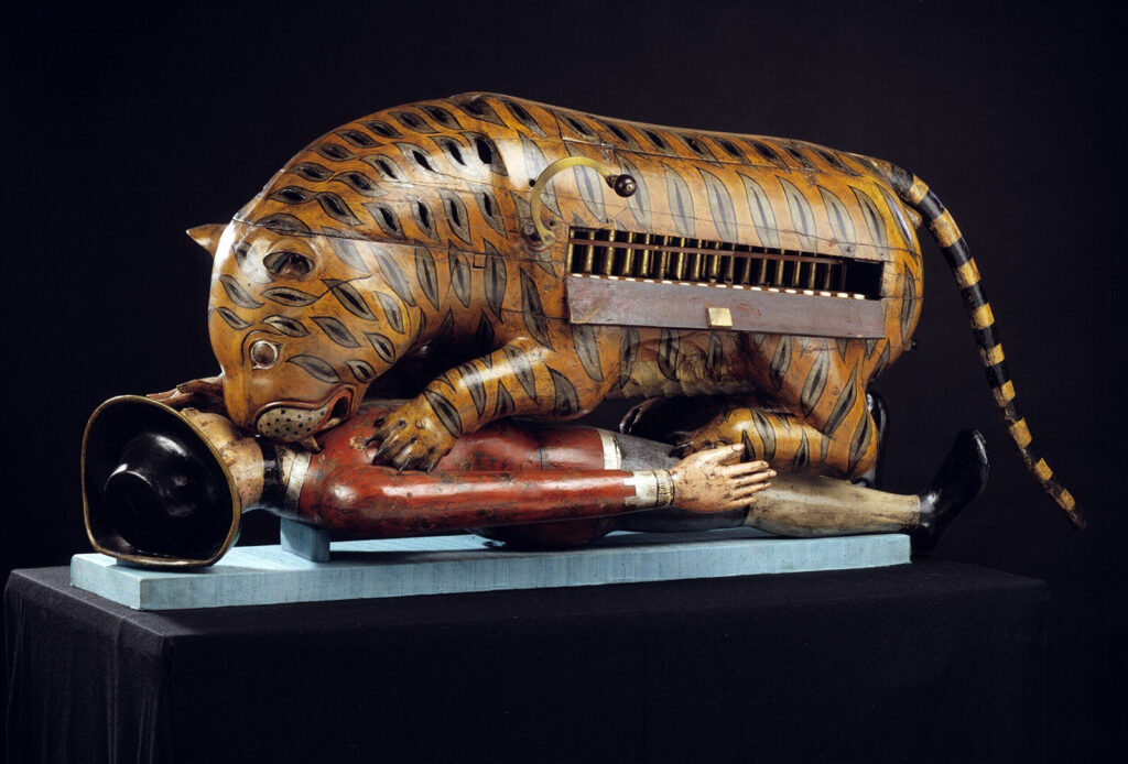 Wooden figure of a tiger mauling a man in a red uniform.