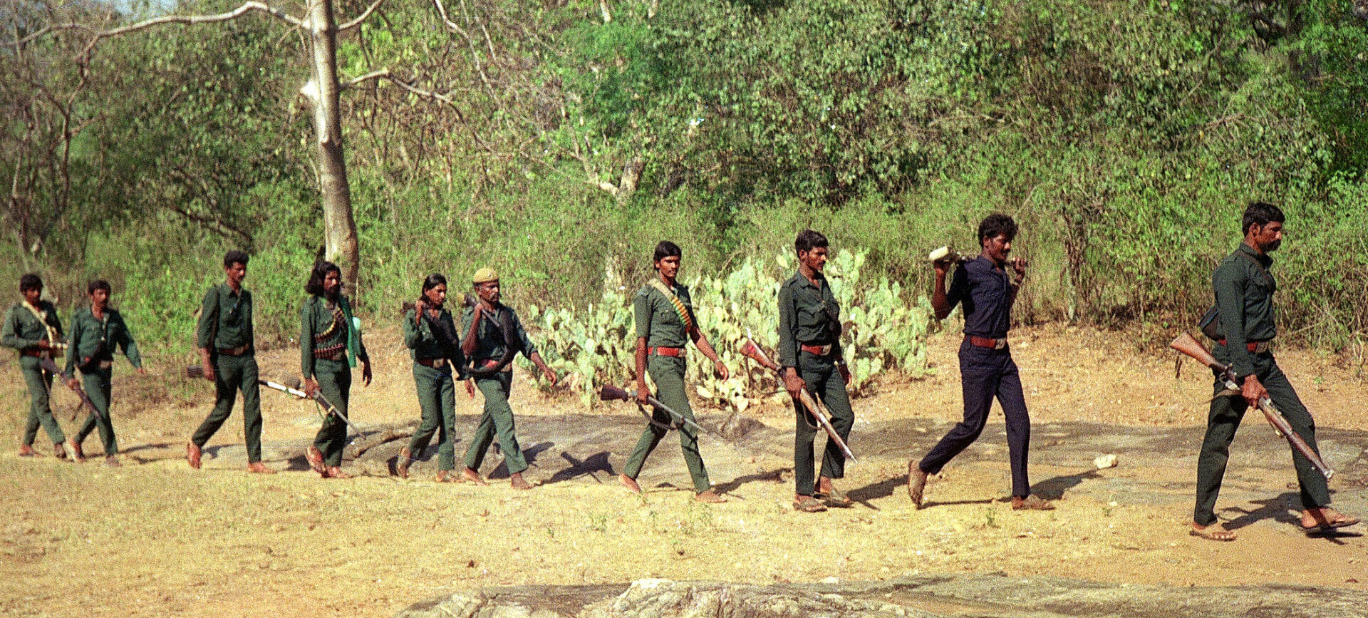 Line of ten armed men in green camo walking in single file