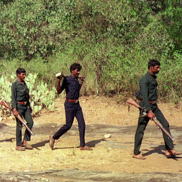 Line of ten armed men in green camo walking in single file