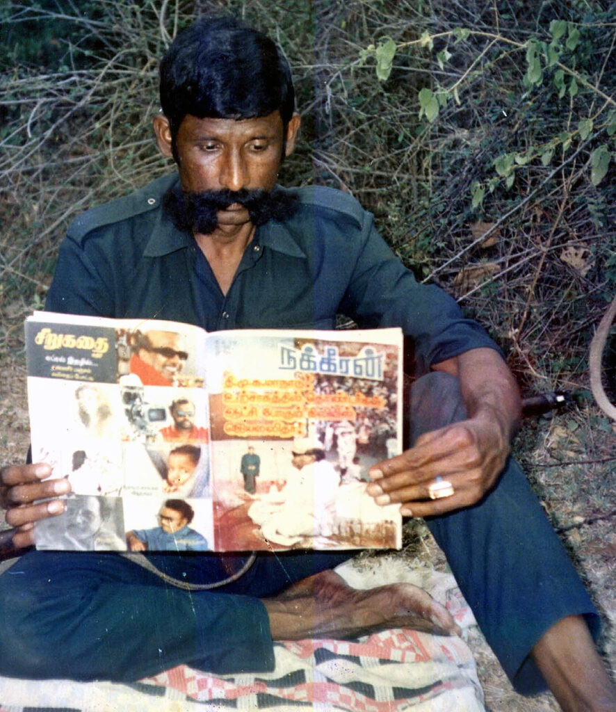 Man sitting on a blanket in a forest reading a colorful magazine