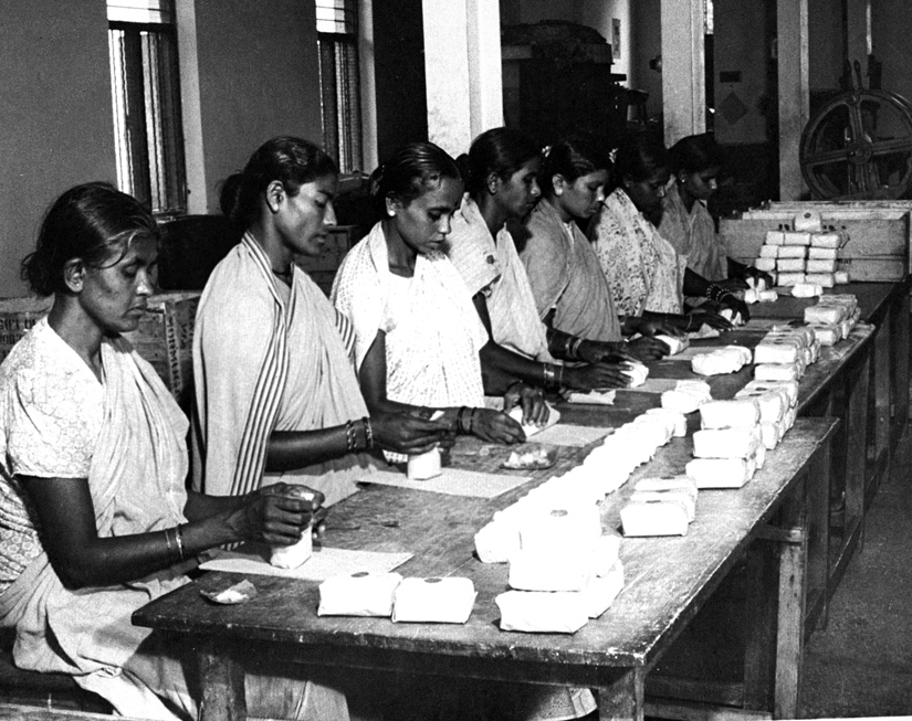 Seven women seated at a table wrapping bars of soap