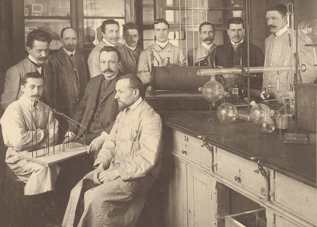 group photo of men in a lab wearing suits and lab coats