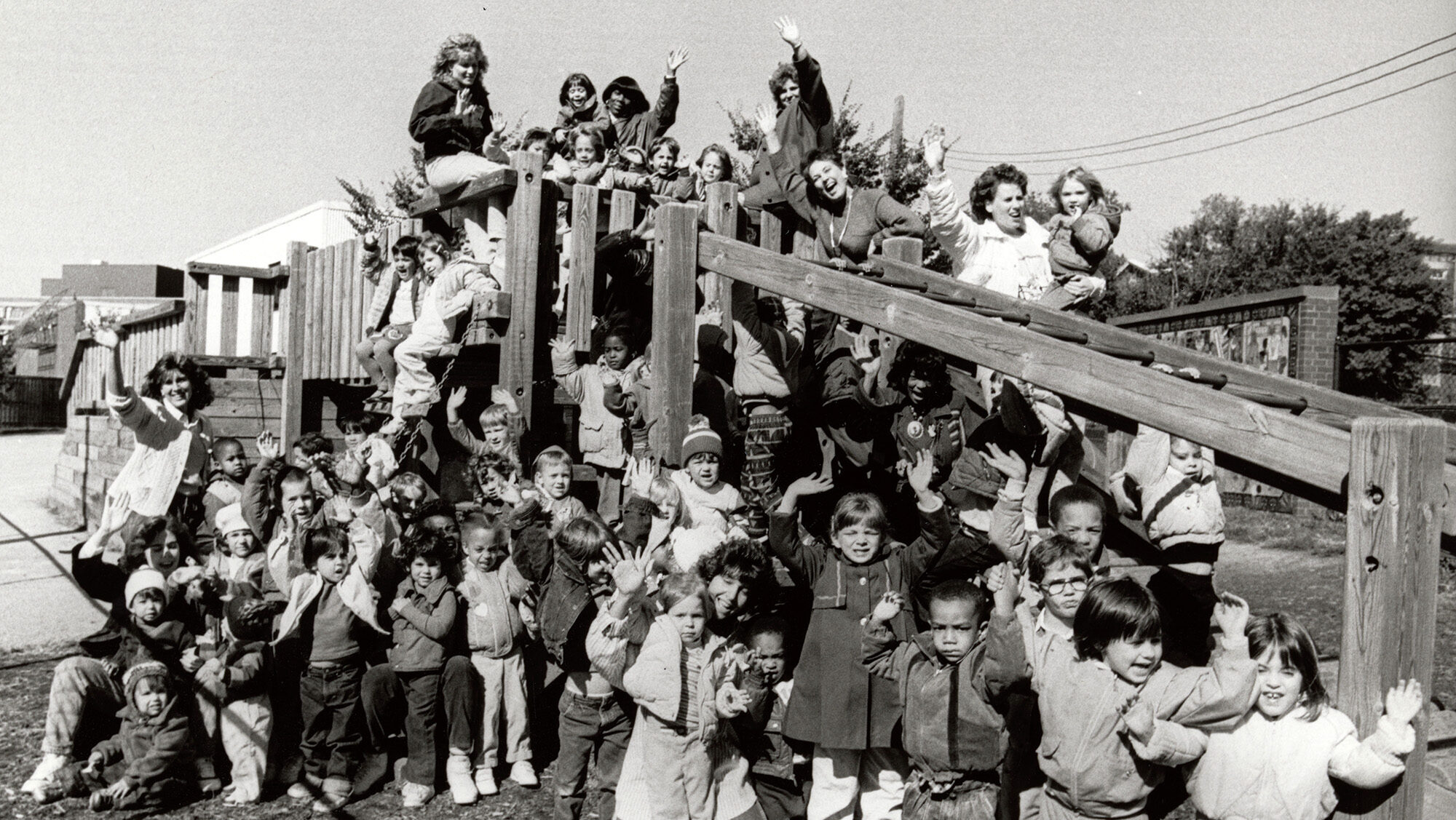 Large group of children and women posing for a photograph on a jungle gym.
