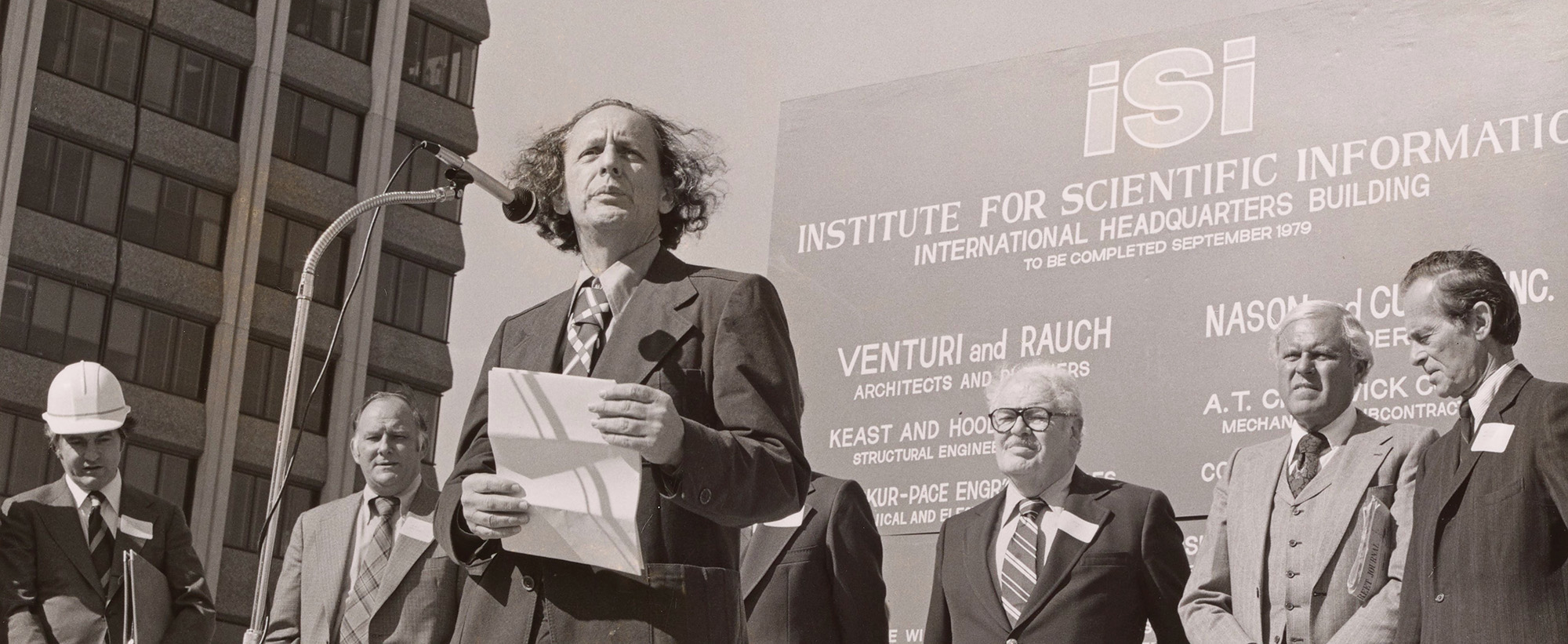 Man reading a speech at a podium with men standing behind him.