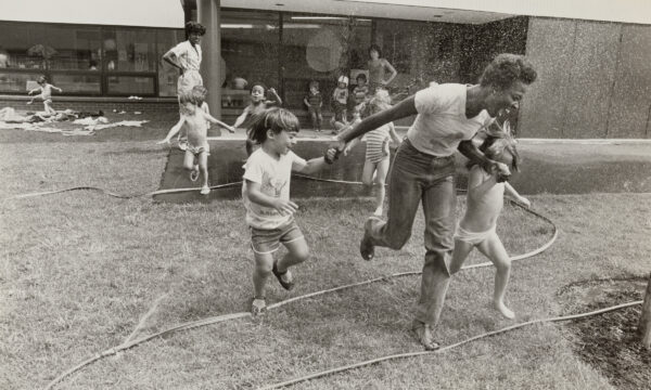 Women and children playing outdoors with a garden hose.