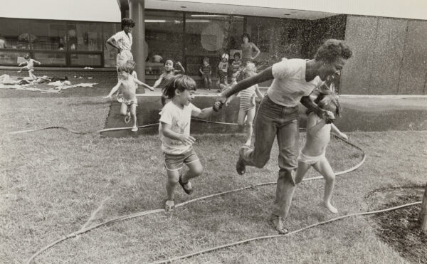 Women and children playing outdoors with a garden hose.