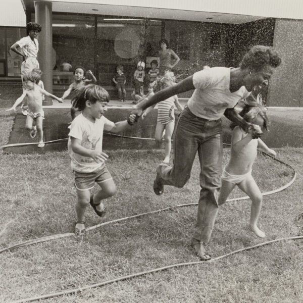 Women and children playing outdoors with a garden hose.