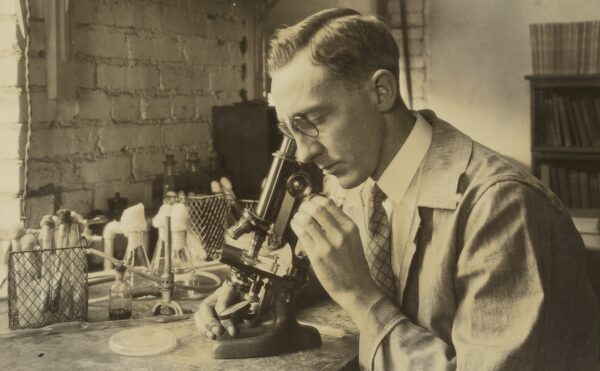 sepia-toned photo of a man looking into a microscope