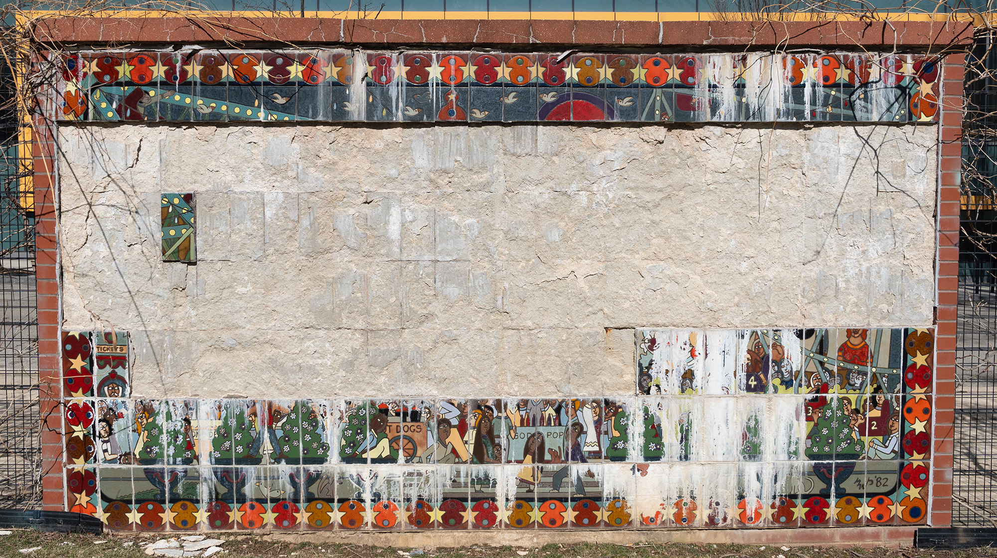 Outdoor mural with tiles missing and vegetation encroaching on the corners.
