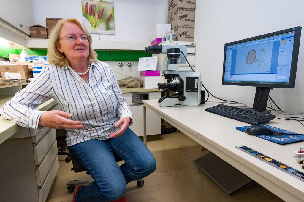 Woman sitting in a lab by microscope and monitor with an enlarged image of pollen
