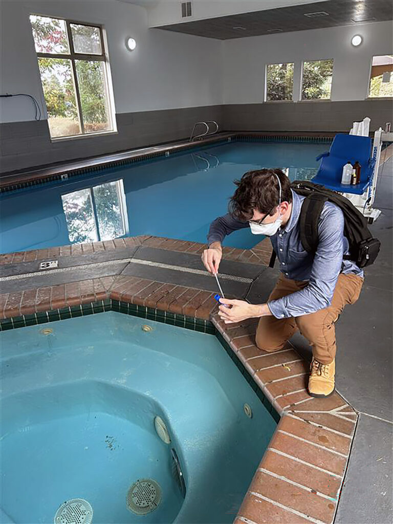 Man crouched over an indoor hot tub sampling water with a pipette.