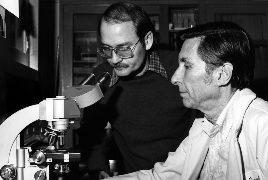 Two men working with a microscope on a table.